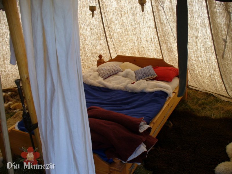 Blick auf ein rekonstruiertes Holzbett in einer hypothetischen Feldlagersituation. Im Hintergrund hngende Tranlampen