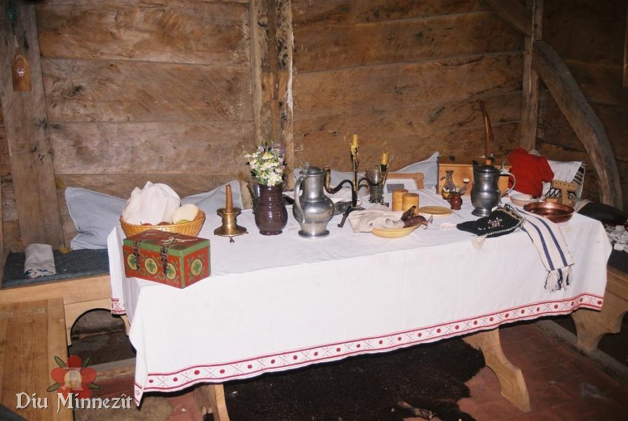 Tisch in der Kammer mit bestickter Decke und Gegenständen alltäglichen Gebrauchs