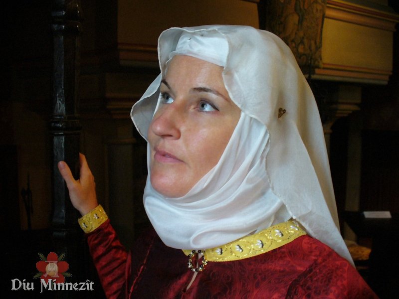 Nicole Perschau in prächtiger hochmittelalterlicher Kleidung mit Zierstickereien am Saum und Edelsteinbesetzter Fibel